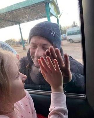 Ein Kind drückt seine Hand gegen das Fenster eines Autos, während eine andere Person von außen lächelt und ebenfalls die Hand auf das Fenster legt. Die Szene vermittelt ein Gefühl von Nähe und Verbindung. (Text KI generiert)