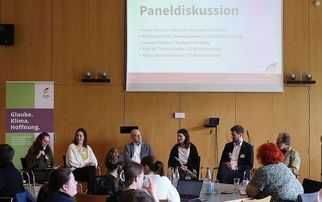Eine Paneldiskussion mit sechs Personen auf der Bühne, die in einem Konferenzraum sitzen. Im Hintergrund ist eine Präsentation zu sehen, die das Thema "Paneldiskussion" anzeigt. Im Vordergrund sind Teilnehmer, die aufmerksam zuhören. Ein Banner mit den Worten "Glaube. Klima. Hoffnung." ist sichtbar. (Text KI generiert)