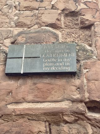 Eine Tafel aus Stein, die an einer Mauer befestigt ist. Darauf steht in großen Buchstaben: "Thy will be done in GOVERNMENT. God be in my plans and in my deciding." Die Schrift ist in einer eleganten Schriftart gestaltet. (Text KI generiert)