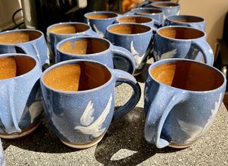 Eine Gruppe von blauen Tassen mit weißen Vogelmotiven steht auf einer dunklen Oberfläche. Die Tassen sind aus Keramik und haben einen glänzenden Innenraum. (Text KI generiert)